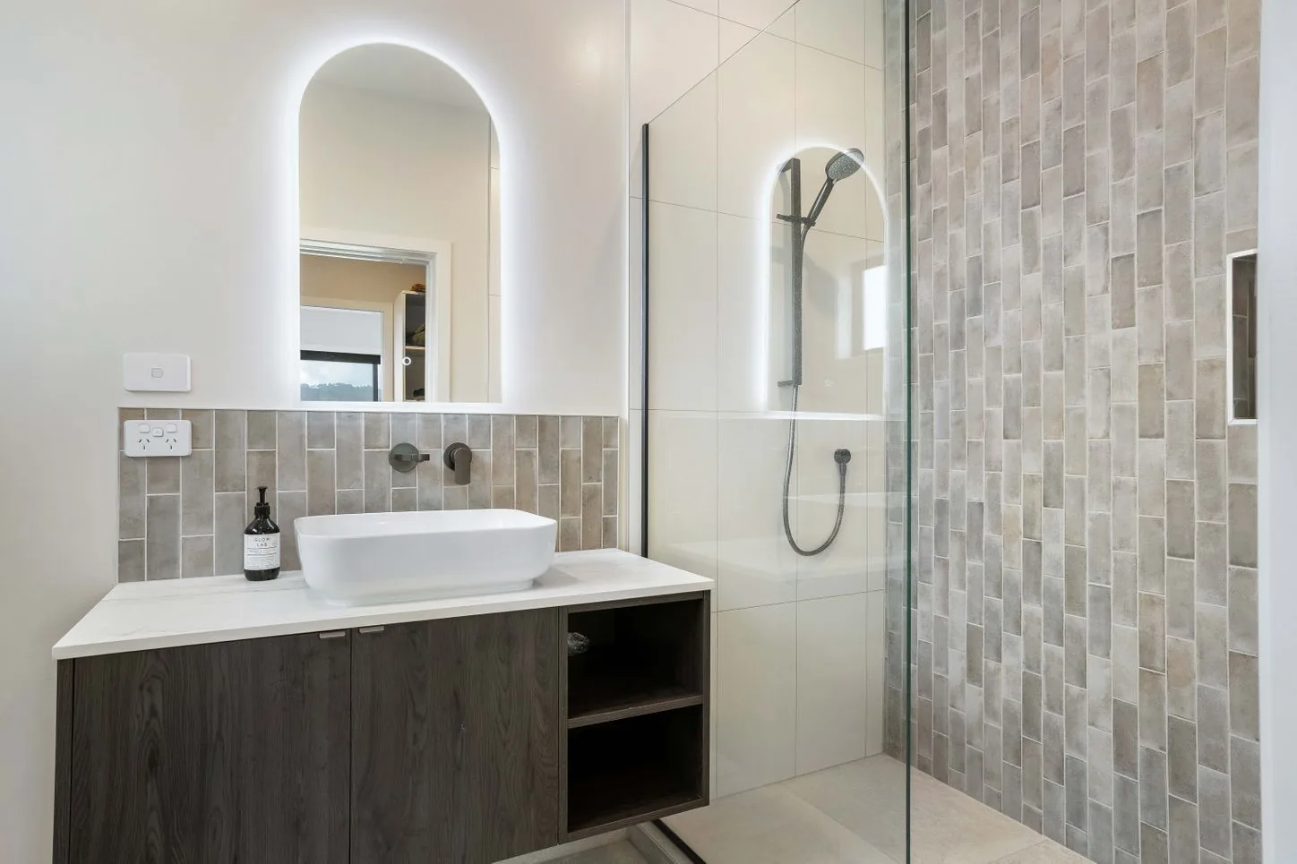 Bathroom with floating vanity, arched backlit mirror and tiled shower