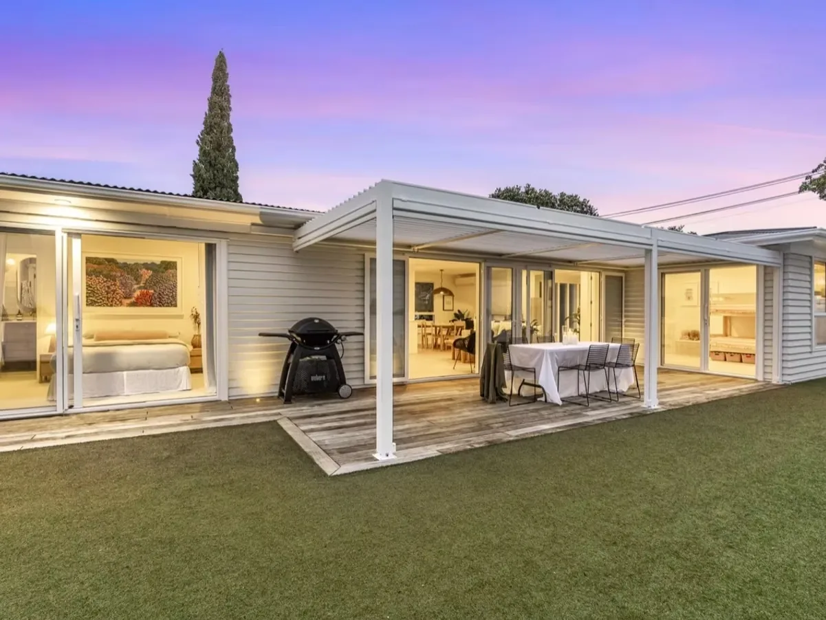 Louvred pergola over a timber deck at dusk beside a white weatherboard house