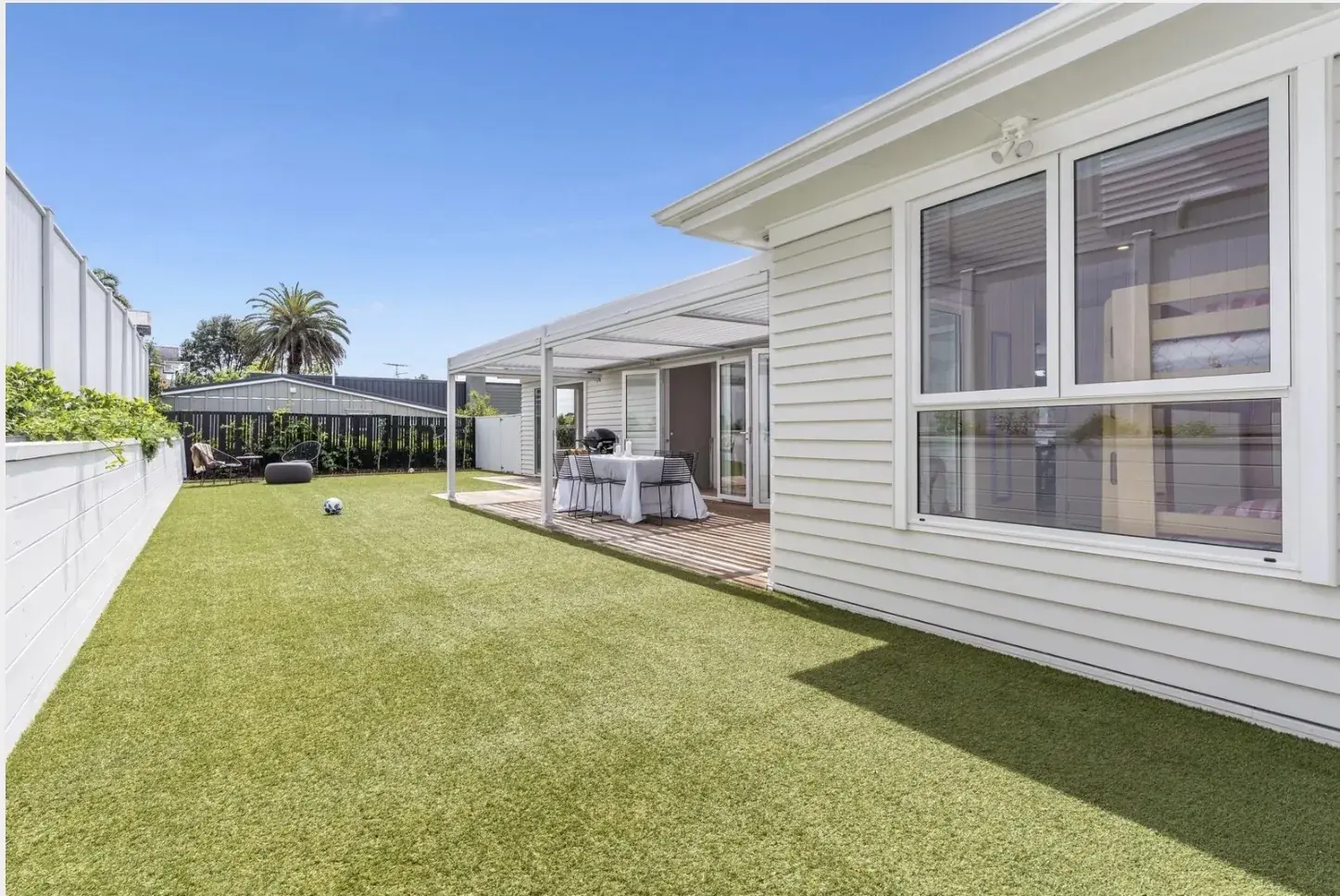 White weatherboard house with a louvred pergola and a timber deck